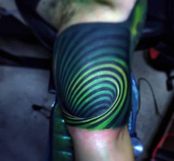 Tattoo of concentric, swirling green and black lines on a person's shoulder, creating a 3D tunnel effect