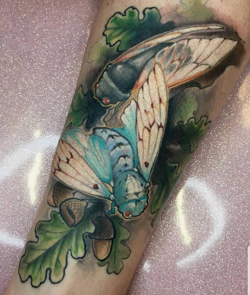 Tattoo of two cicadas in vibrant colors on a person's forearm, surrounded by leaves