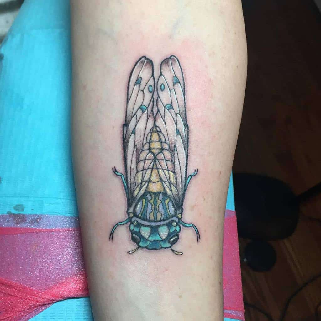 Forearm with detailed cicada tattoo in black, blue, and yellow ink
