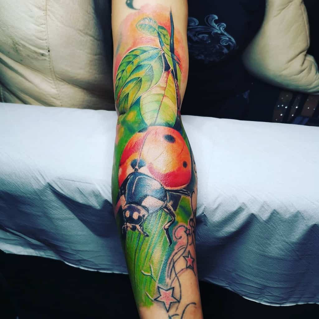 Vibrant full-sleeve tattoo featuring a large, detailed ladybug on a leaf with rich green, red, and orange hues, creating a realistic effect.