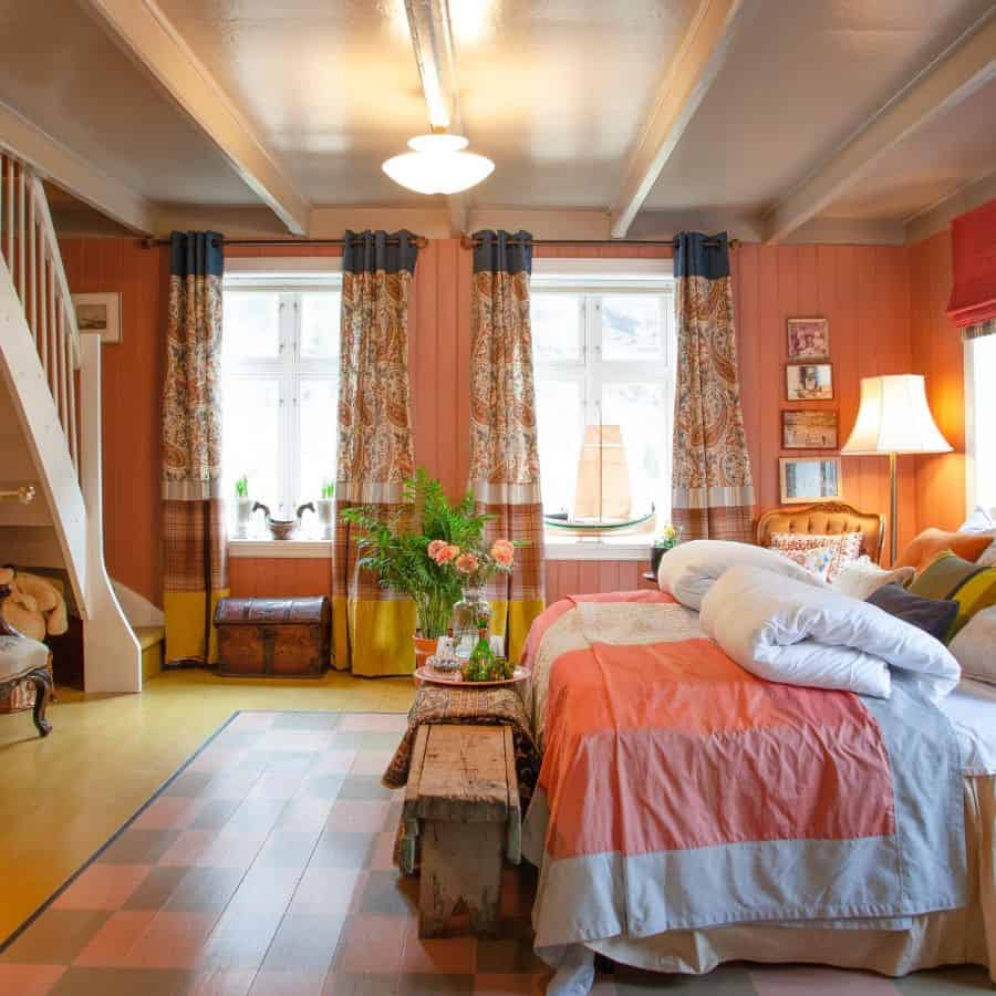 Cozy bedroom with colorful decor, a double bed, patterned curtains, lamp, and wooden bench in a rustic setting