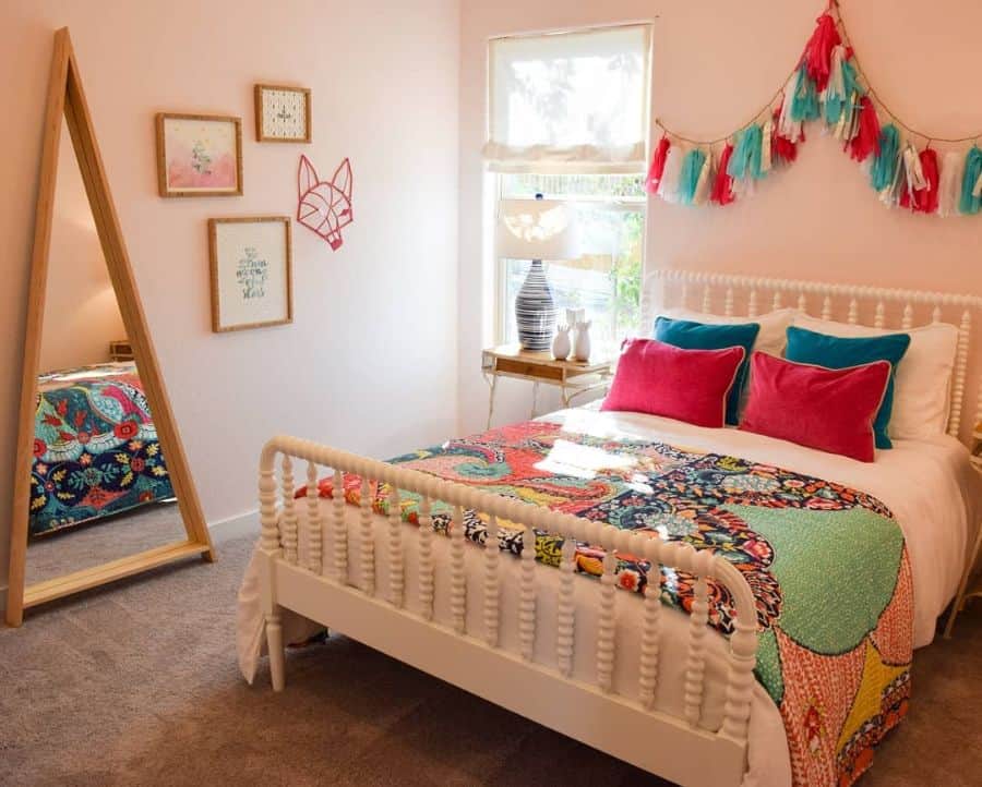 Colorful bedroom with a patterned quilt, pink and blue pillows, wall decor, mirror, and decorative garland