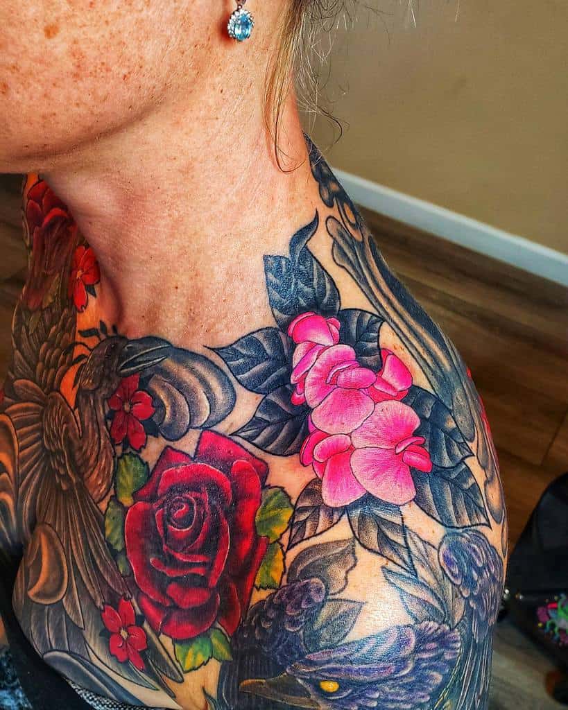 Woman with intricate floral tattoos adorning her shoulder and chest, showcasing vibrant red roses, delicate pink flowers, and dark leaves