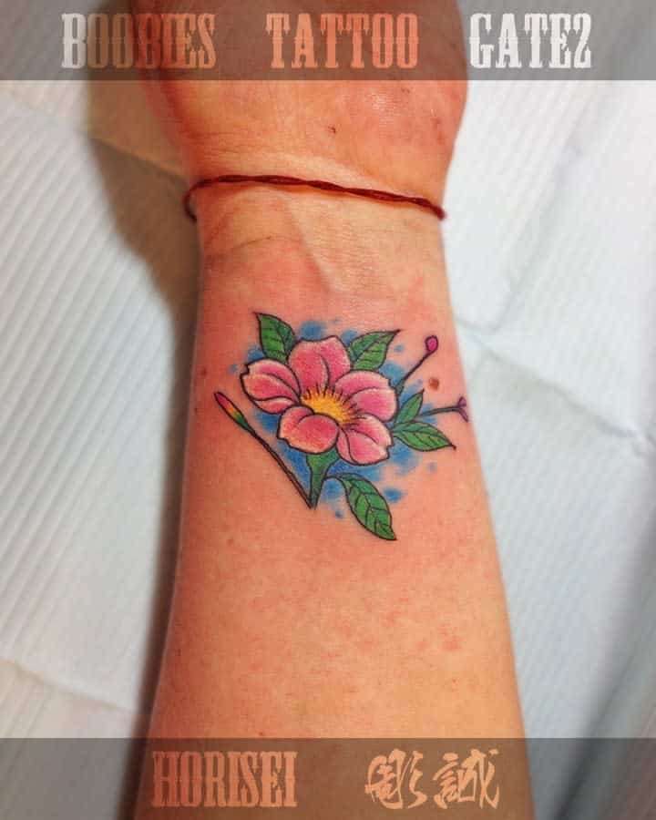 Colorful flower tattoo with green leaves elegantly winding down to the wrist on an arm