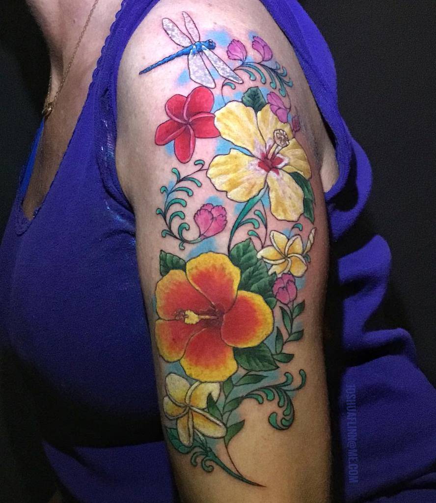 Upper arm tattoo featuring colorful hibiscus and plumeria flowers, a dragonfly, and swirling green vines with pink buds