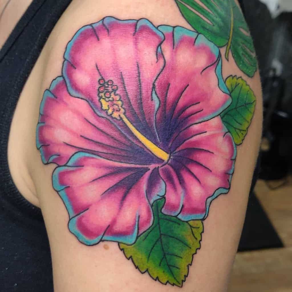 A colorful hibiscus flower tattoo with green leaves on an upper arm