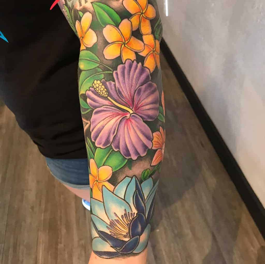 Colorful floral sleeve tattoo with hibiscus and frangipani on an arm