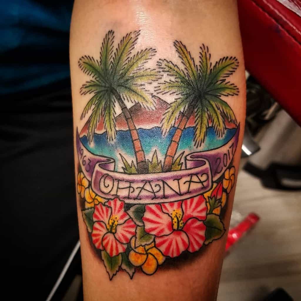 Colorful tattoo of two palm trees, "Ohana," with hibiscus flowers and the years 1963 and 2017