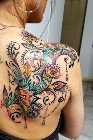 Vibrant back tattoo featuring colorful floral patterns, intricate black lace details, and ornamental swirls for a bold and elegant look.