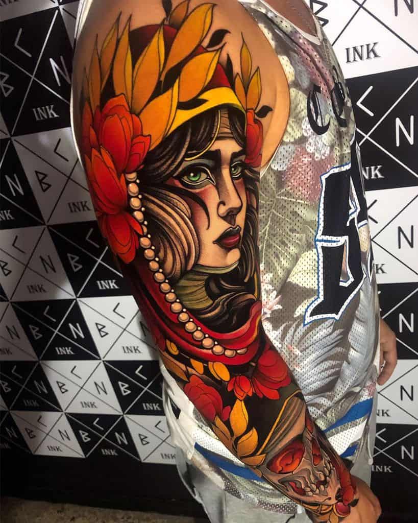 Vibrant full-sleeve tattoo of a gypsy woman with piercing green eyes, bold red and gold floral details, and intricate shading.