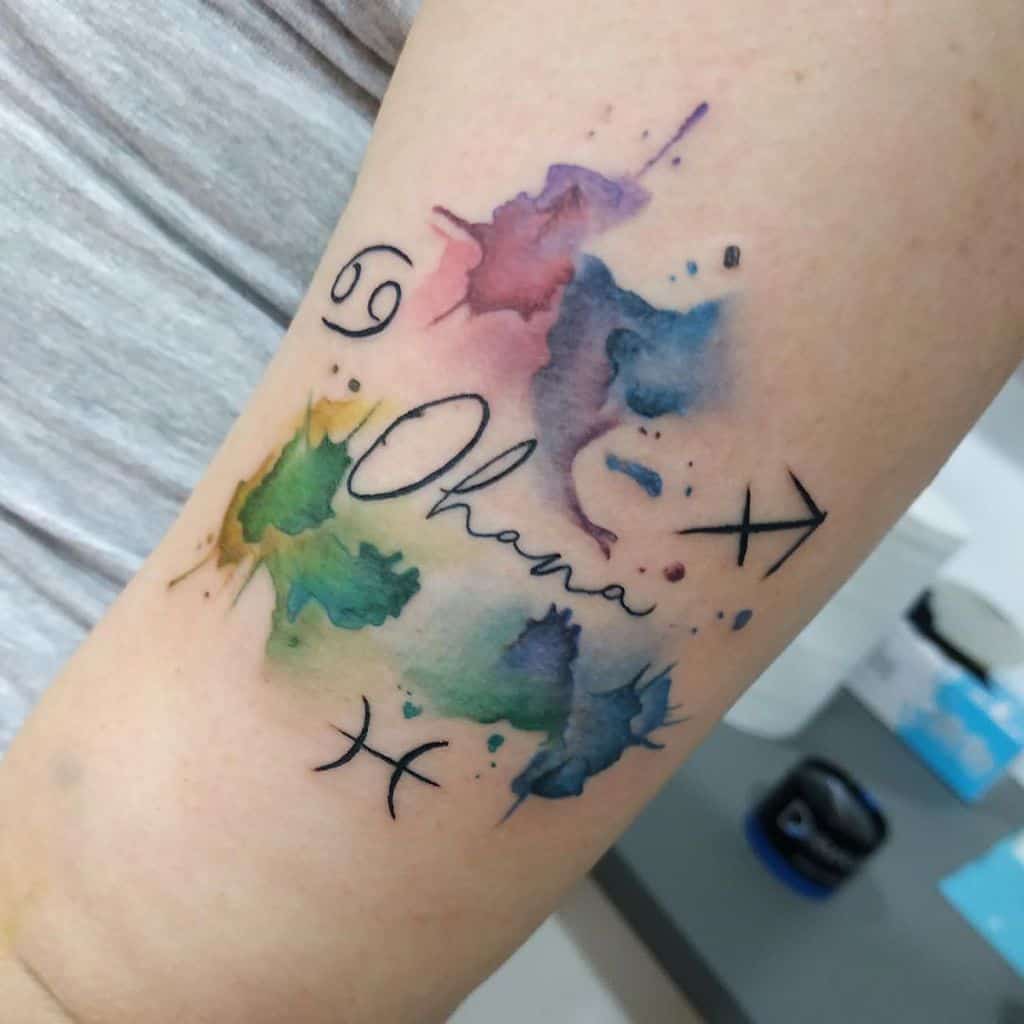Vibrant watercolor tattoo with 'Ohana' and zodiac symbols, representing family, individuality, and cosmic connection.