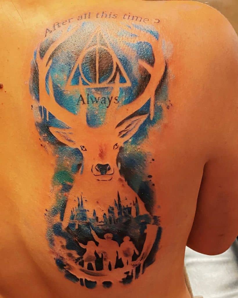 Large back tattoo featuring a stag Patronus, Deathly Hallows symbol, Hogwarts silhouette, and 'After all this time? Always' quote in blue hues.