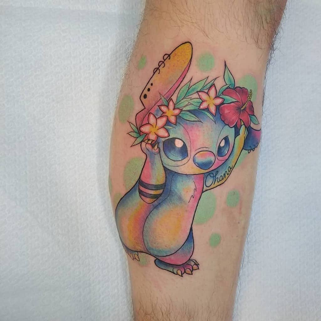 Colorful tattoo of Stitch from Lilo & Stitch wearing a flower crown, with the word 'Ohana' written below, on the forearm.