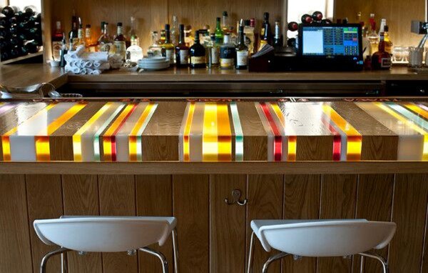 Vibrant bar top with colorful resin stripes, paired with white seating and a well-stocked bar.