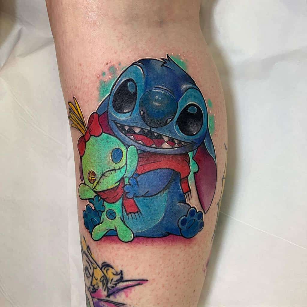 Colorful tattoo of Stitch from Lilo & Stitch hugging Angel, with both wearing scarves, on the upper arm.