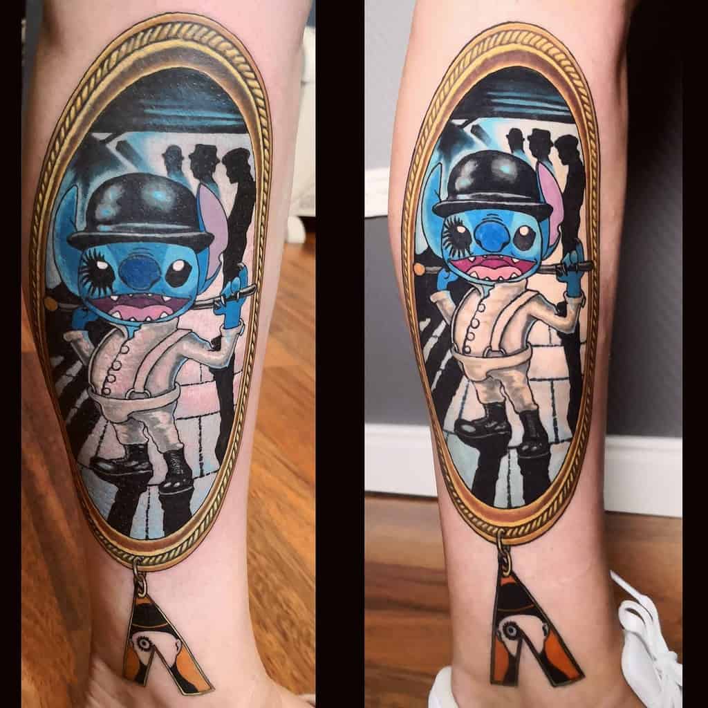 Colorful tattoo of Stitch from Lilo & Stitch wearing a bowler hat and suit, depicted in a surreal mirror frame, with an abstract, black and white background, on the forearm.