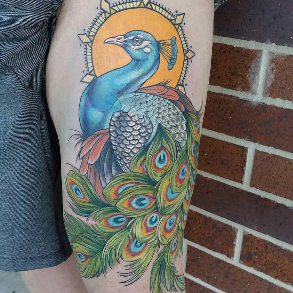 Colorful peacock tattoo with vibrant tail feathers in blue, green, and orange, framed by a sunburst background on the upper arm.