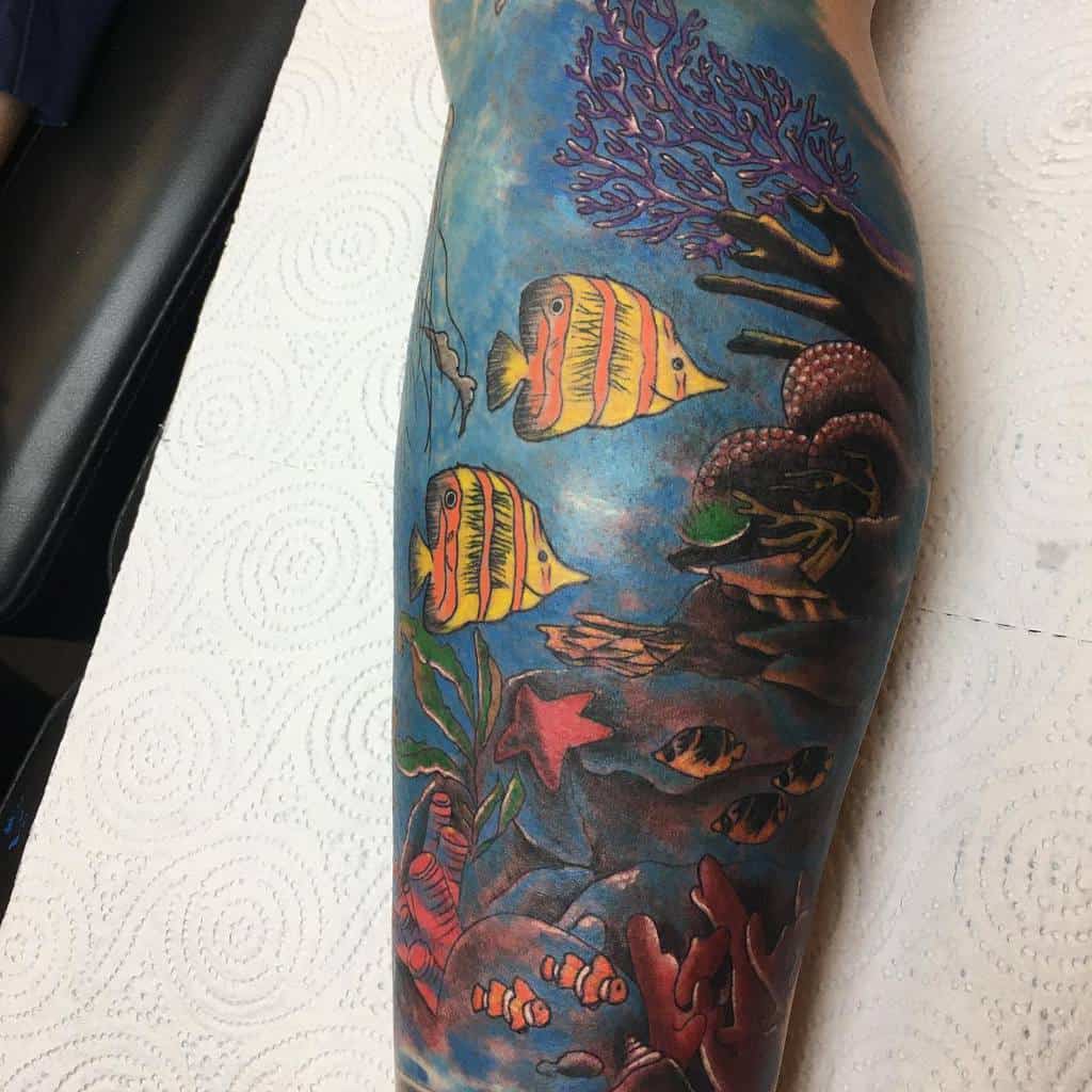 Colorful underwater scene leg sleeve tattoo featuring fish, star fish, rocks, coral, and sea plants 