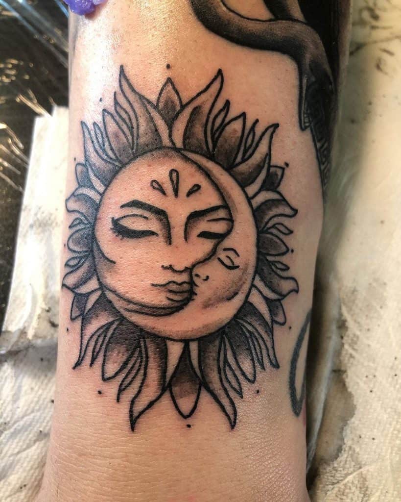 Black ink tattoo of a sun and moon intertwined, with serene faces, delicate shading, and bold rays creating a celestial balance.