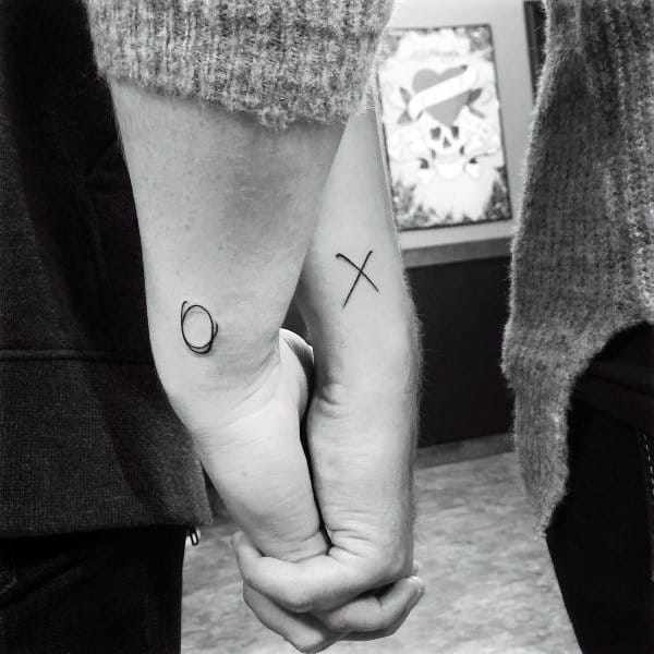 Simple matching tattoos of an X and O on forearms, representing hugs and kisses shared between the couple.