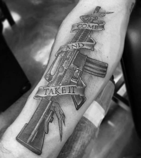 Black and grey AR-15 tattoo with a "Come and Take It" banner wrapped around the rifle, symbolizing defiance, gun rights, and resilience.