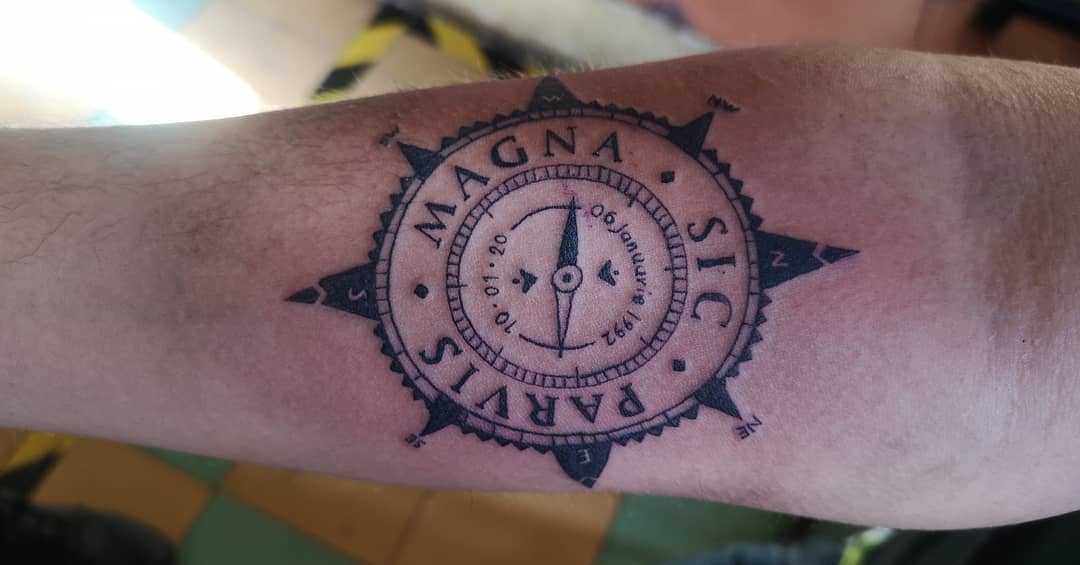 Tattoo of a compass design with the text "MAGNA SIC PARVIS" on an arm