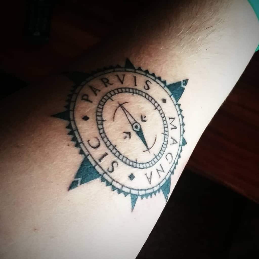 Tattoo of a compass with the words "Sic Parvis Magna" on the forearm
