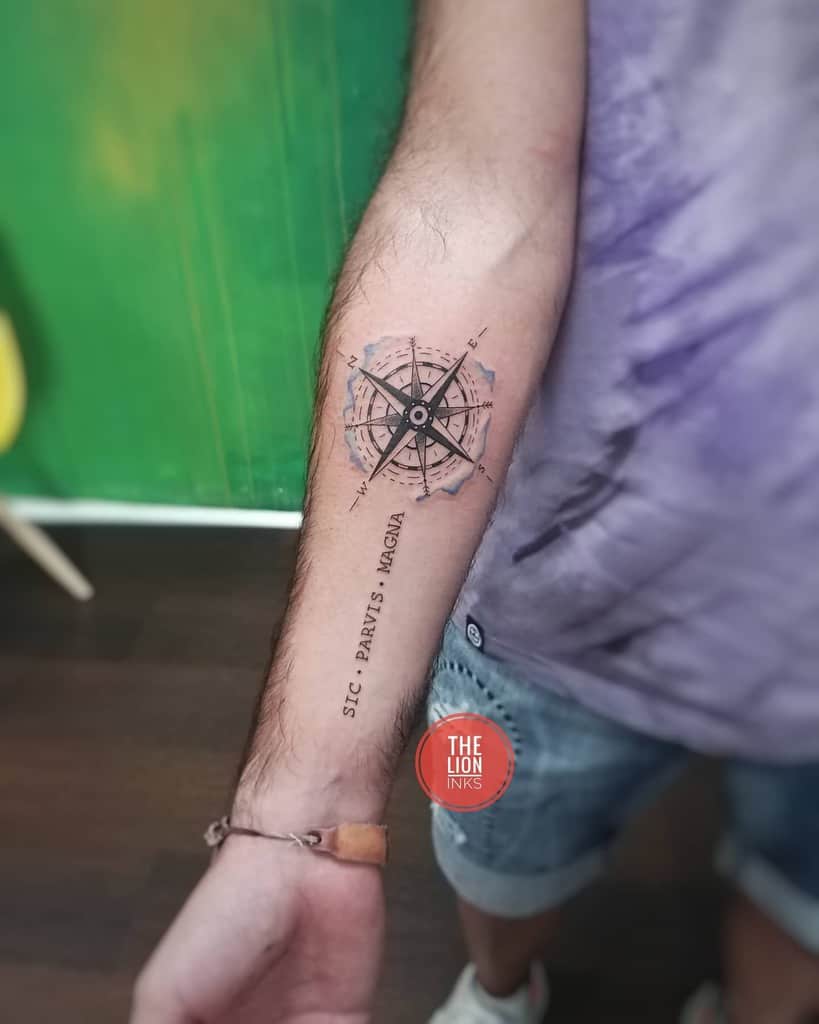 Forearm tattoo of a compass with 'Sic Parvis Magna' text, featuring detailed map accents and fine black ink work