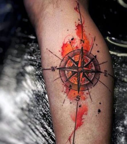 A tattoo of a compass with a red and orange watercolor background on a person's arm