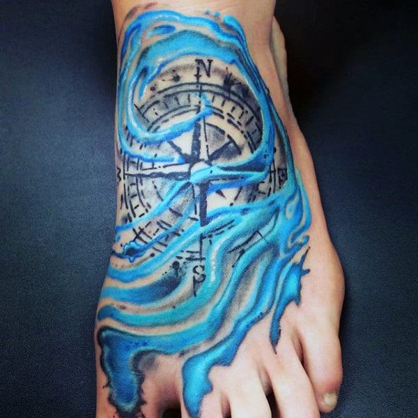 A foot tattoo featuring a compass surrounded by blue waves on the top of a foot