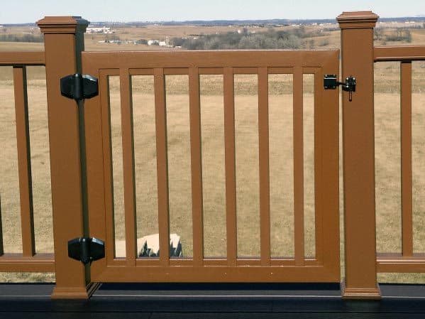 Brown wooden gate with vertical slats and hinges, leading to a vast field deck