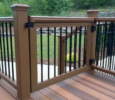 Brown wooden gate with black metal bars on the deck, overlooking lawn and garden