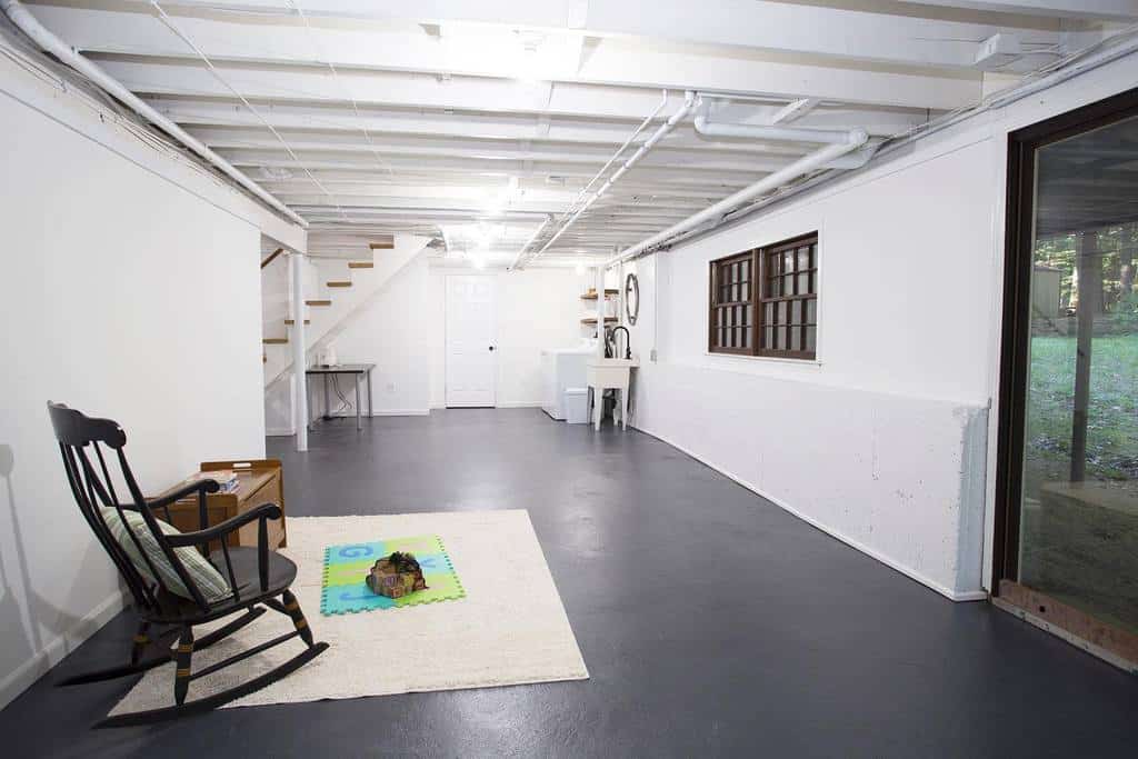 Large minimalist basement with exposed beams, concrete floor, and a rocking chair setup.