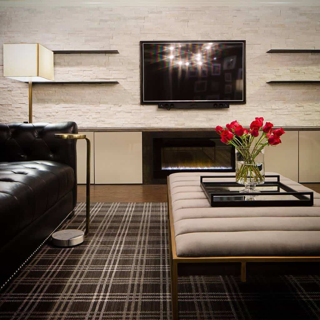 Modern basement living area with black leather couch, mounted TV, and ottoman with red flowers.