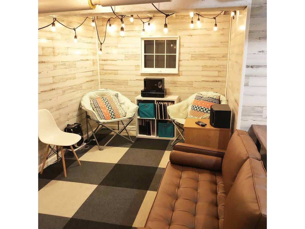 Cozy small basement room with string lights, lounge chairs, and a brown leather couch.