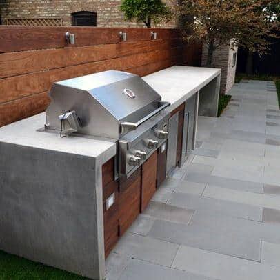 Outdoor kitchen featuring a built-in stainless steel grill, wooden cabinets, and a concrete countertop on a tiled patio