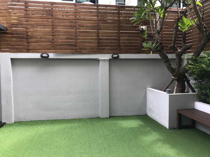 Modern backyard with wooden fence, concrete wall, and artificial grass flooring.