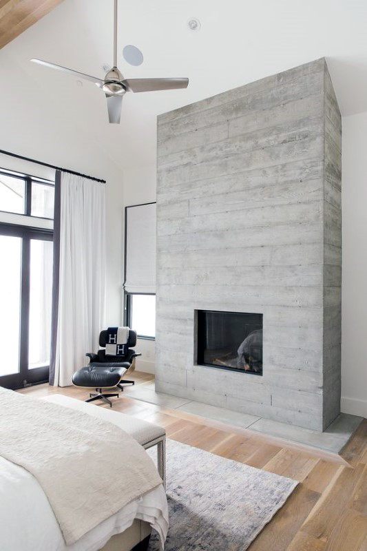 Board-formed concrete fireplace in a bright bedroom with wooden floors and modern furnishings.