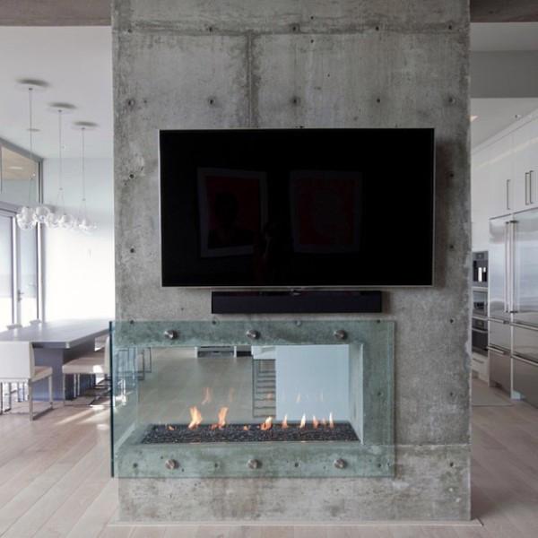 Modern concrete fireplace with glass enclosure and wall-mounted TV in a sleek open-plan space.