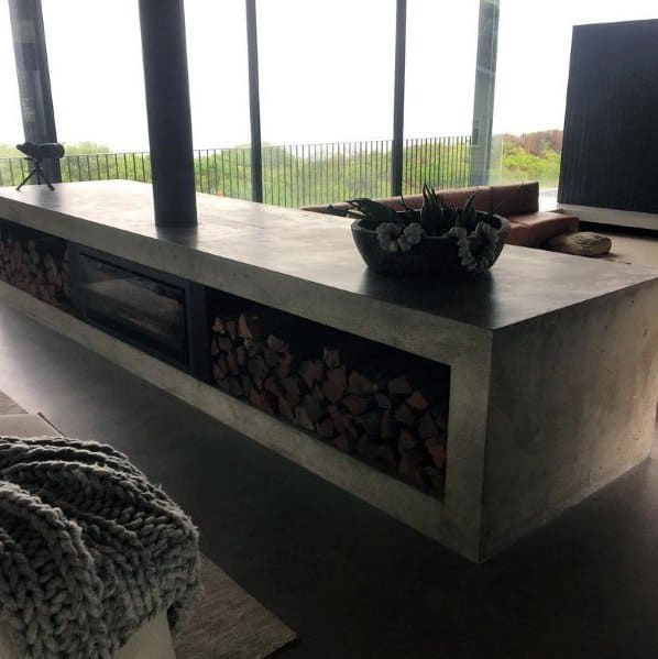 Modern concrete fireplace with integrated wood storage and panoramic glass window backdrop.