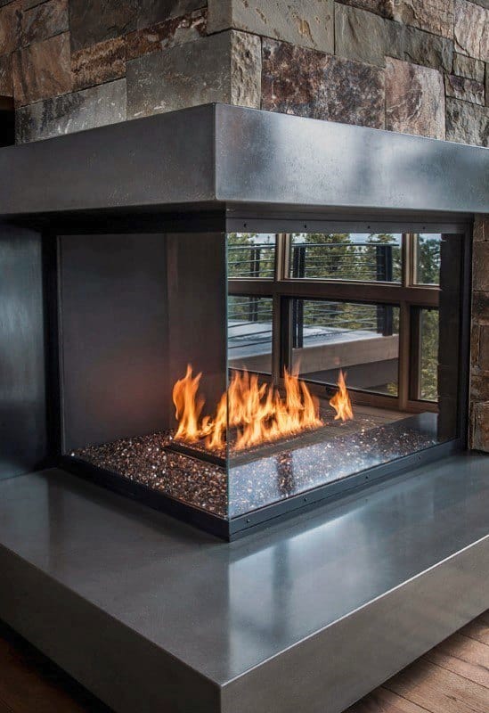 Modern glass-enclosed fireplace with polished concrete base and stone wall backdrop.