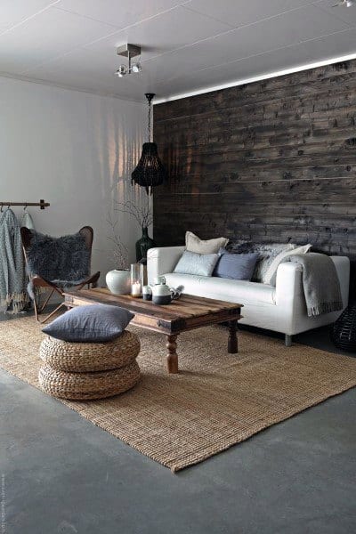 Cozy living room with white sofa, rustic wooden table, woven poufs, textured gray wall, and concrete floor
