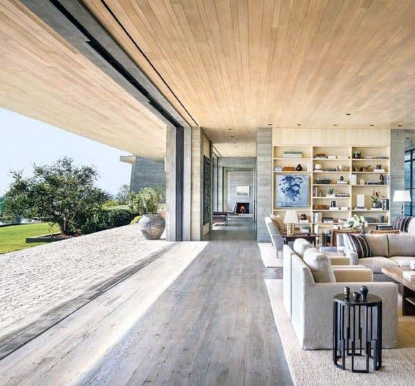 Spacious, modern living room with sliding glass doors, concrete floor, wooden ceiling, and open view to a green outdoor area