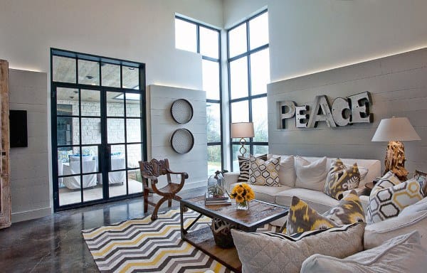 Modern living room with a "PEACE" sign, decorative pillows, zigzag rug, large windows, and concrete floor