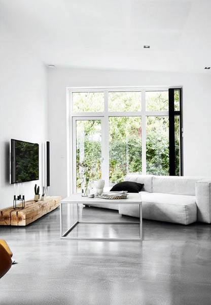 Minimalist living room with white sofa, large windows, TV, wooden table, and a sleek concrete floor