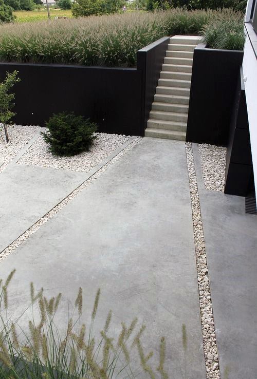 Modern concrete pathway with stairs, black retaining walls, and ornamental grass landscaping.