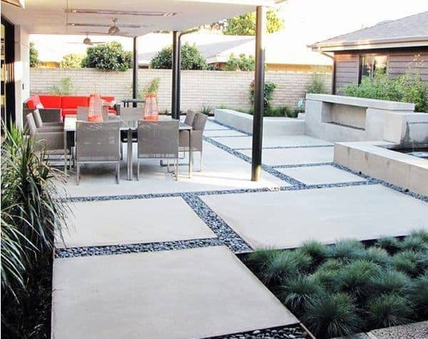 Modern patio featuring concrete slabs, gravel accents, patio dining set, and lush landscaped greenery