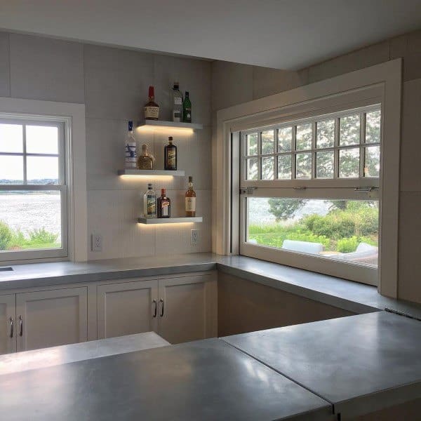 Modern home bar with concrete countertop and illuminated shelves near large windows.