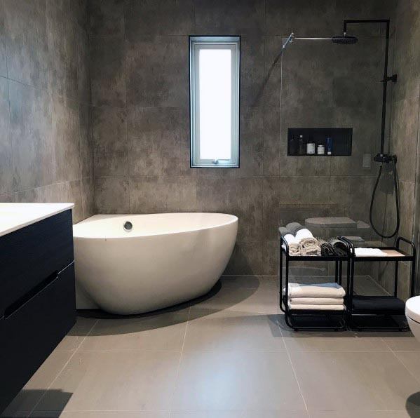 A modern bathroom with gray concrete walls, a sleek freestanding bathtub, and a glass-enclosed shower.