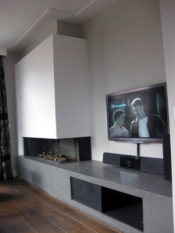 Modern corner fireplace with white surround, TV setup, and sleek concrete bench design.